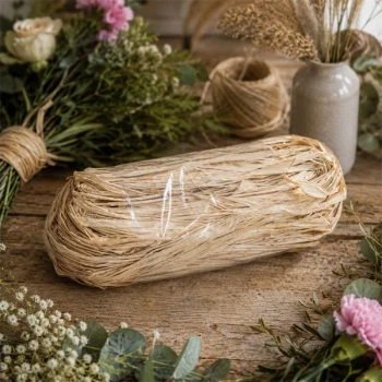 Naturlig bastsnor til buketbinding omgivet af blomster og grønne grene på rustikt træbord. Perfekt til blomsterbinding, dekorationer og kreative projekter.