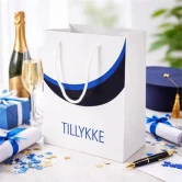 Blå student gavepose med teksten Tillykke på festbord med champagne, gaver og studenterhue