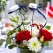 Blomsterpind med blå studenterhue placeret i blomsterdekoration med røde roser og hvide blomster som bordpynt til studenterfest.