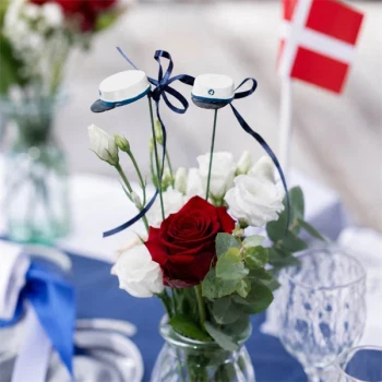 Blomsterpinde med blå studenterhuer i blomsterdekoration med røde og hvide blomster på festbord til studenterfest.