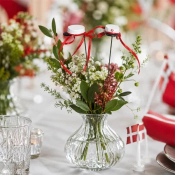 Blomsterpinde med røde studenterhuer i blomsterdekoration på festbord med Dannebrog til studentergilde.