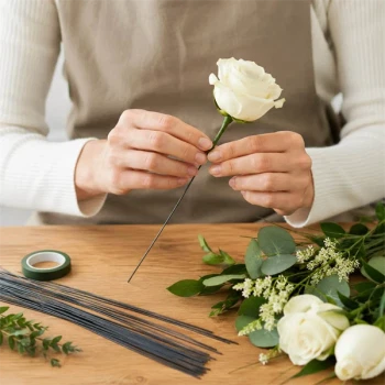 Person anvender blomsterpinde i metal 0,80 mm til blomsterbinding af en hvid rose på arbejdsbord med blomster og grønt.