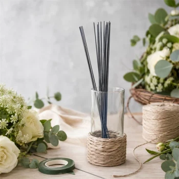 Blomsterpinde i metal 0,80 mm placeret i glasvase omgivet af blomster, eucalyptus og blomsterbinderudstyr på kreativt arbejdsbord.