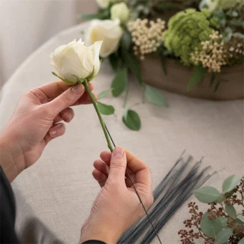 Person bruger blomsterpind i metal 1,20 mm x 30 cm til blomsterbinding af en hvid rose. Ideel til blomsterdekorationer, kranse og kreative hobbyprojekter.