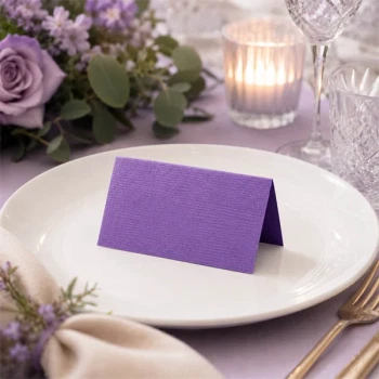 Lilla tekstureret bordkort placeret på festbord med tallerken blomster og lys til bryllup eller konfirmation