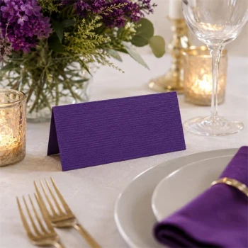 Mørk lilla tekstureret bordkort på elegant festbord med blomster og borddækning til bryllup