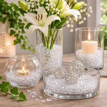Klart dekorationsglas i glasvaser og skåle med hvide liljer, levende lys og sølvkugler som elegant borddekoration.