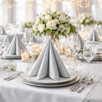 Elegant festbord med sølvfarvede Airlaid servietter, hvid dug, lys, blomster og glas i klassisk borddækning