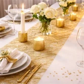 Elegant festbord pyntet med guldfarvet sizoweb bordløber, stearinlys og hvide blomster