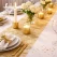 Elegant festbord pyntet med guldfarvet sizoweb bordløber, stearinlys og hvide blomster