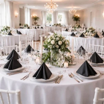 Elegant festlokale med runde borde dækket i hvidt og sorte foldede servietter, blomsterdekorationer og stearinlys