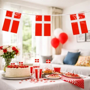 Flagguirlande med Dannebrog flag ophængt over festbord med kage, balloner og dansk borddækning til fødselsdag