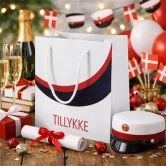 Rød student gavepose med teksten Tillykke omgivet af studenterhuer, champagne, gaver og danske flag ved studenterfest