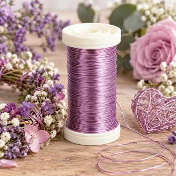 Lavendellilla myrtetråd 0,50 mm på spole omgivet af lilla og rosa blomster samt dekorativt metaltrådshjerte på træbord.