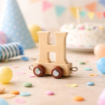 Navnetog bogstav H i naturtræ på bord til børnefødselsdag med farverigt pynt i baggrunden