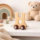 Navnetog bogstav H i naturtræ på hylde i hyggeligt børneværelse med bamse og regnbuelegetøj i baggrunden