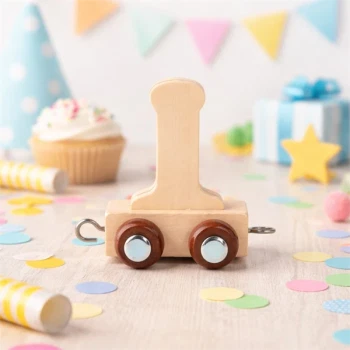 Navnetog bogstav I i naturtræ på bord med farverigt konfetti, cupcake og fødselsdagsdekorationer til børnefødselsdag