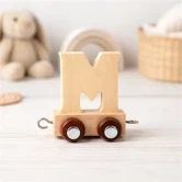 Navnetog bogstav M i naturtræ på togvogn placeret på lyst bord i hyggeligt børneværelse