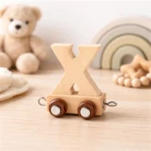 Navnetog bogstav X i naturtræ på træbord med bamse og regnbuelegetøj i baggrunden på børneværelse