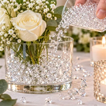 Klare Raindrops dekorationsdråber hældes i glasvase med hvide roser og grønne blade som elegant blomsterdekoration.