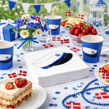 Blå studentservietter med studenterhue på opdækket bord til studenterfest med kage, jordbær og danske flag