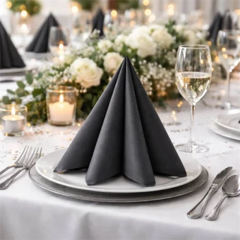 Sort Airlaid serviet foldet i pyramideform på hvid tallerken ved elegant festbord med blomster og stearinlys