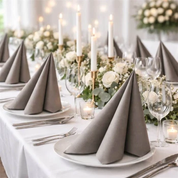 Elegant festbord med gråbrune Sovie Linclass airlaid servietter foldet på hvide tallerkener og blomsterdekorationer