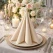 Beige Sovie Linclass airlaid serviet foldet på hvid tallerken med stearinlys, vinglas og blomster på elegant festbord.