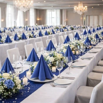 Pyntet festlokale med lange borde dækket i hvidt og blå Sovie Linclass Airlaid servietter foldet til festlig borddækning