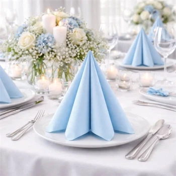 Lyseblå Sovie Linclass Airlaid serviet foldet på elegant festbord med hvide duge, blomsterdekorationer og stearinlys.