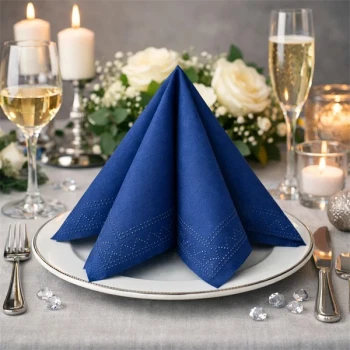 Mørk blå Sovie tissue serviet foldet på hvid tallerken, elegant festbord med lys, blomster og vinglas.